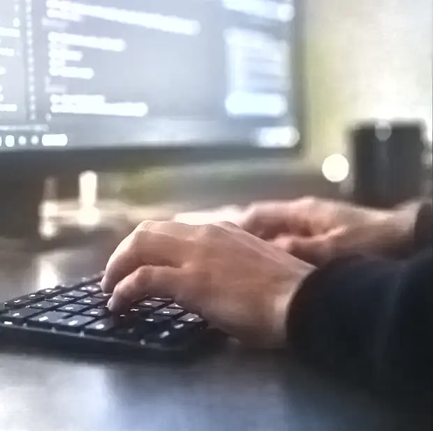 Hands typing on a keyboard lit by a monitor